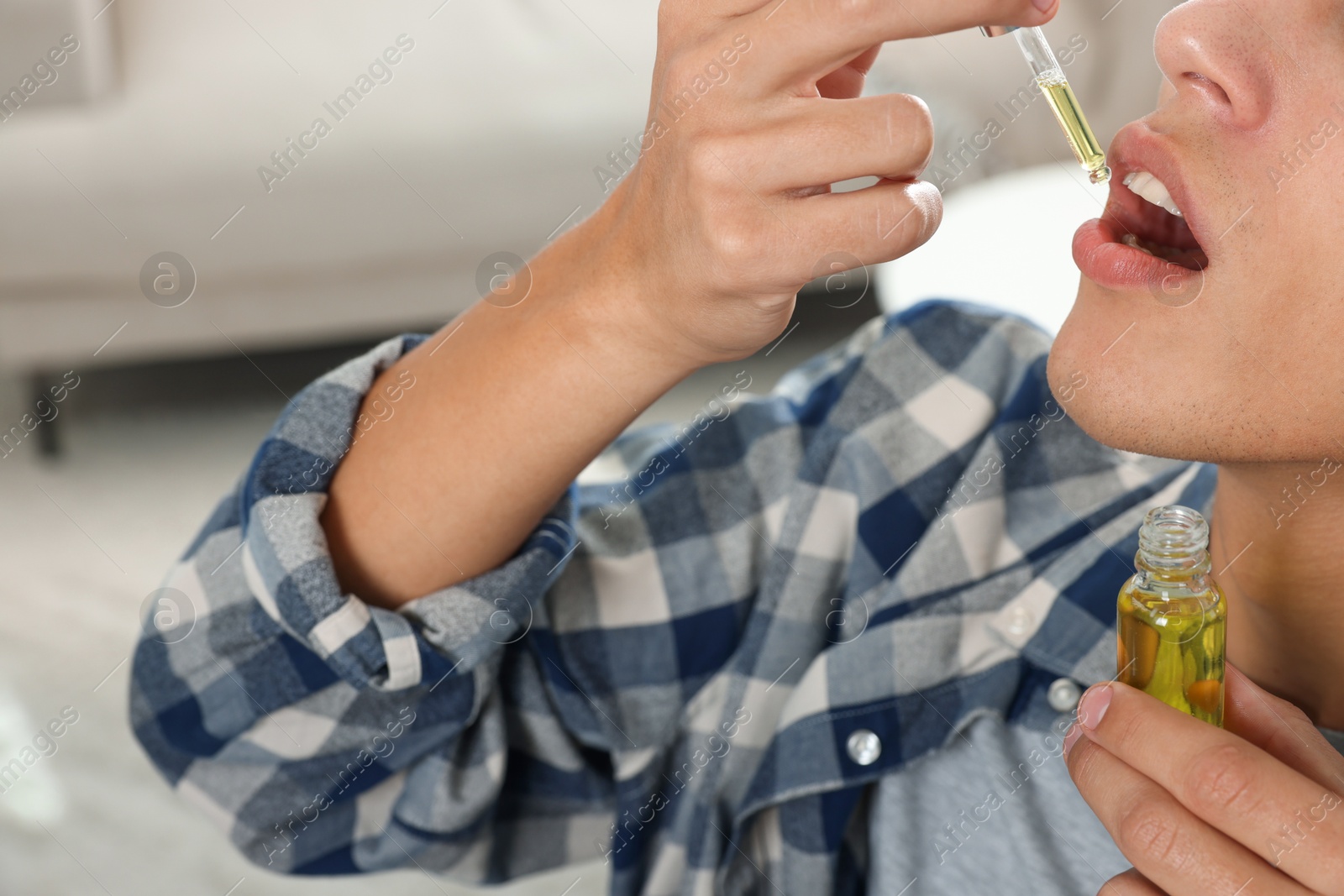 Photo of Young man taking CBD tincture indoors, closeup