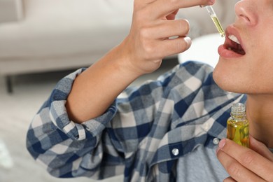 Photo of Young man taking CBD tincture indoors, closeup