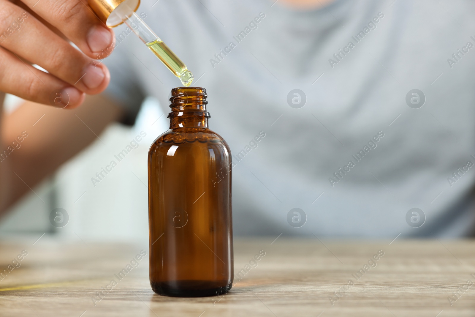 Photo of Young man dripping CBD tincture into bottle from dropper at wooden table, closeup. Space for text