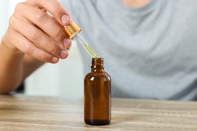 Photo of Young man dripping CBD tincture into bottle from dropper at wooden table, closeup