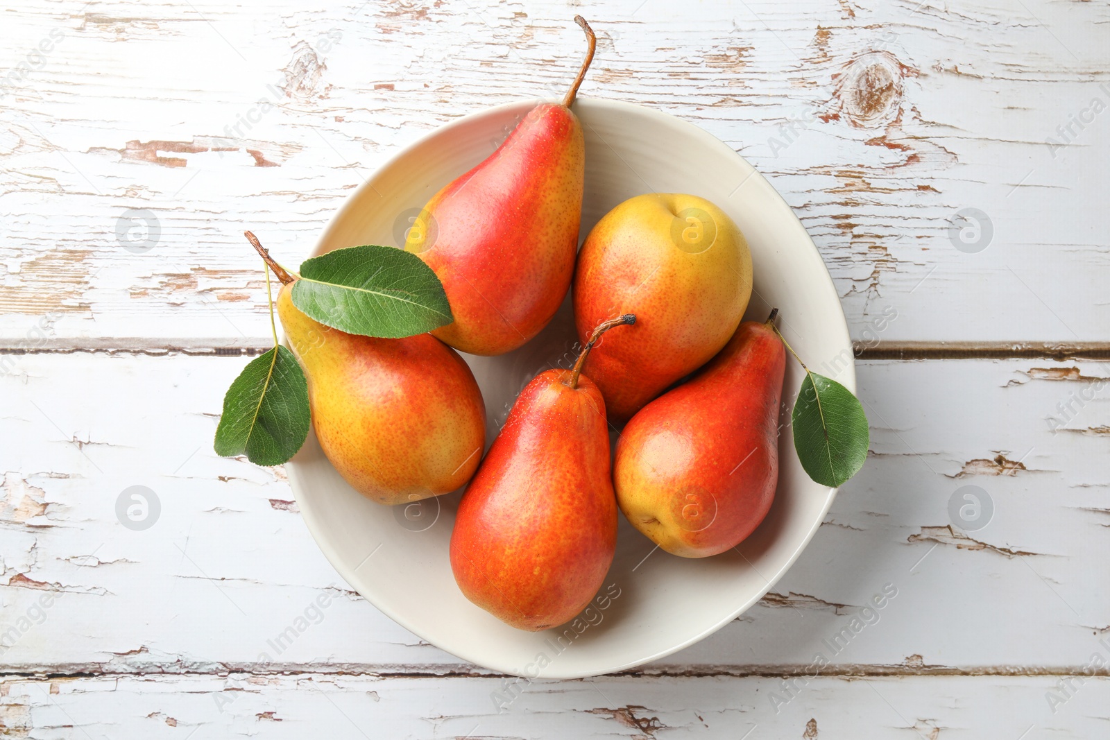 Photo of Ripe juicy pears in bowl on light wooden table, top view