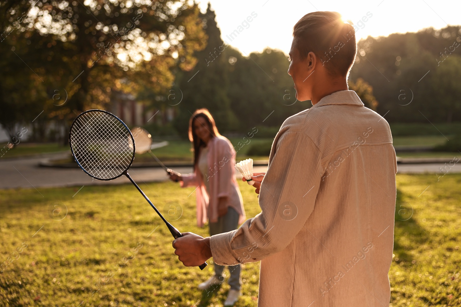 Photo of Young man and woman playing badminton in park on sunny day, selective focus