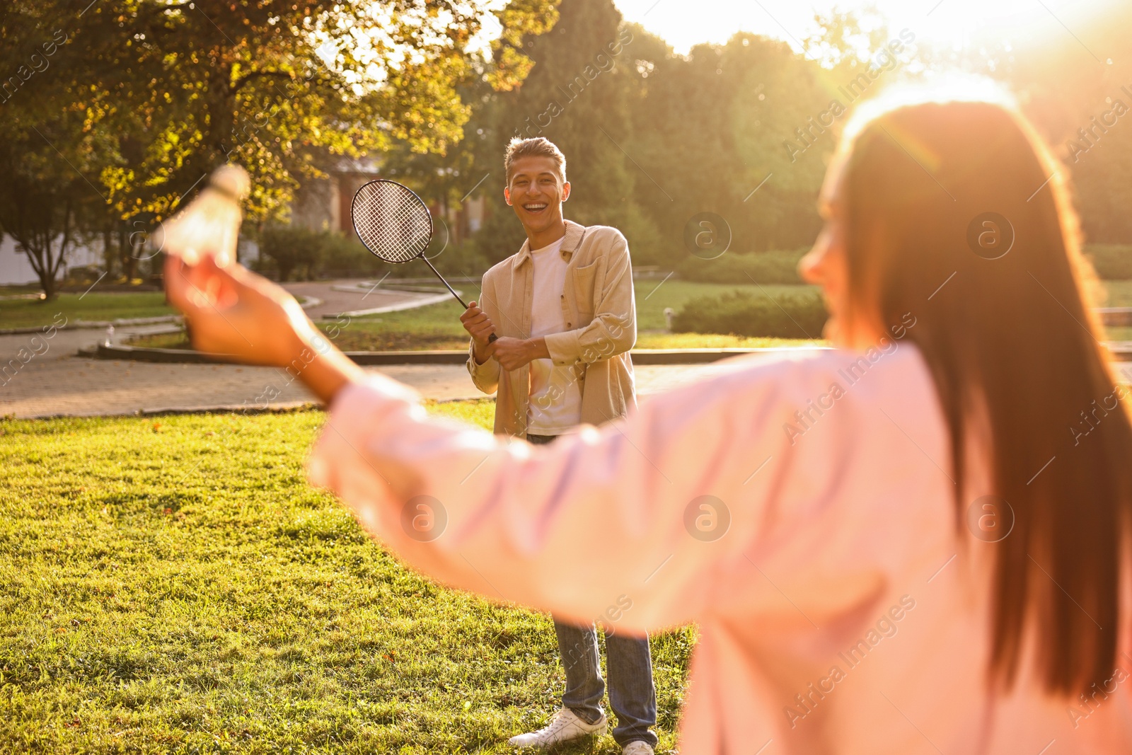 Photo of Young woman and man playing badminton in park on sunny day, selective focus