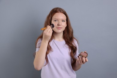 Photo of Teenage girl applying blush with brush on light grey background