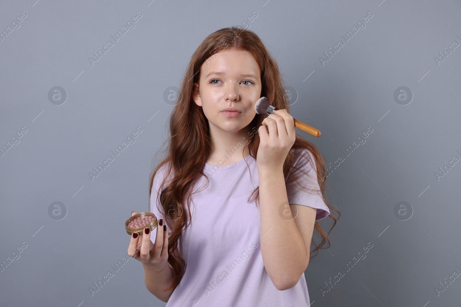 Photo of Teenage girl applying blush with brush on light grey background