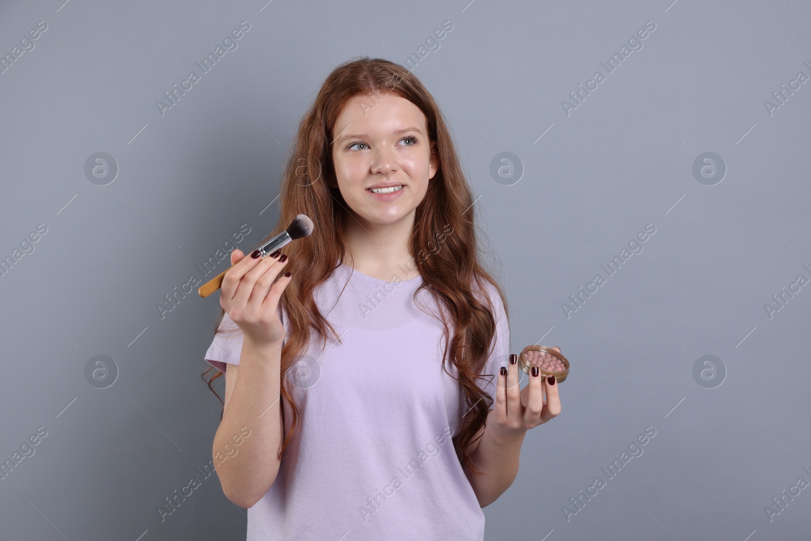 Photo of Teenage girl applying blush with brush on light grey background