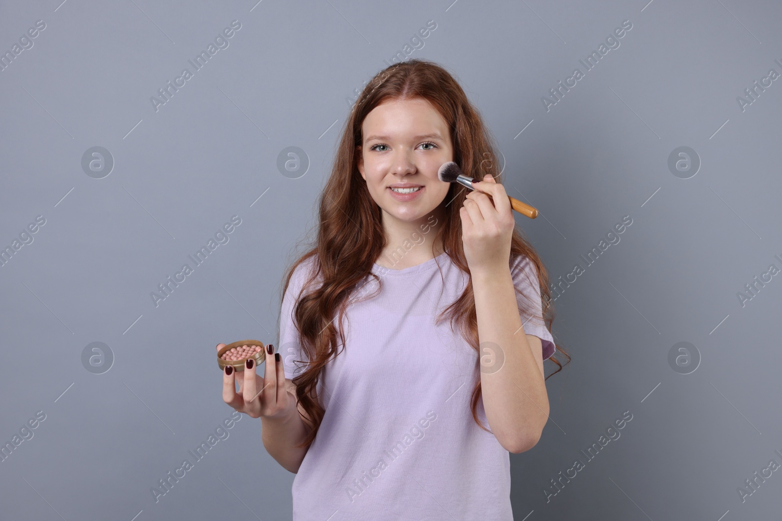 Photo of Teenage girl applying blush with brush on light grey background