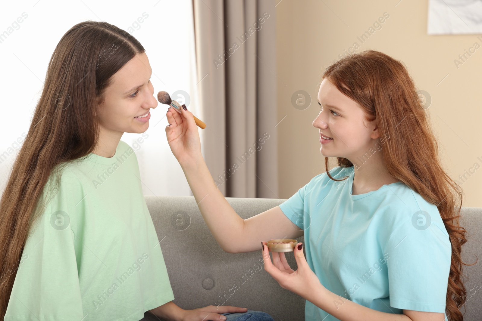 Photo of Teenage girl applying blush on her friend's face indoors