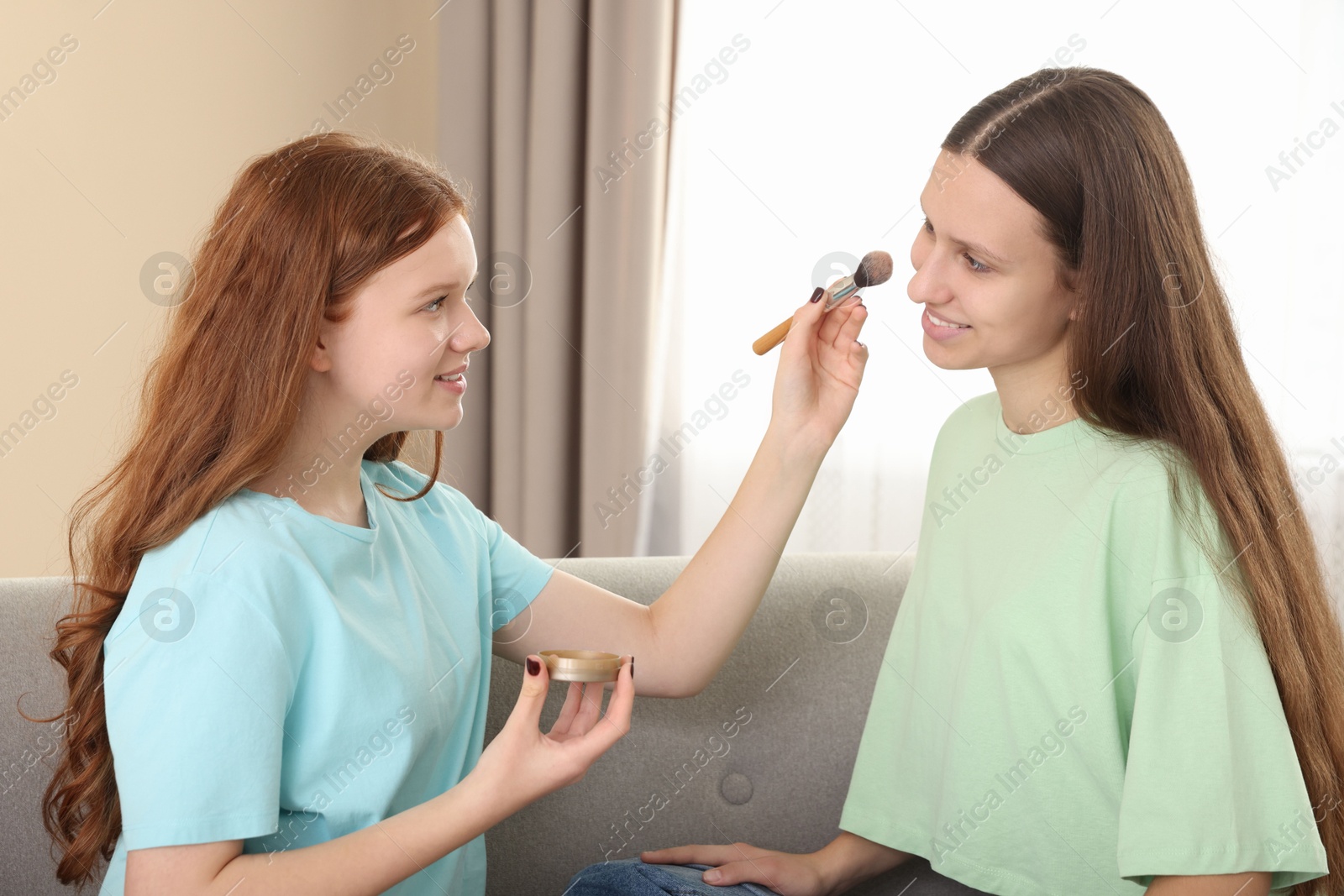 Photo of Teenage girl applying blush on her friend's face indoors