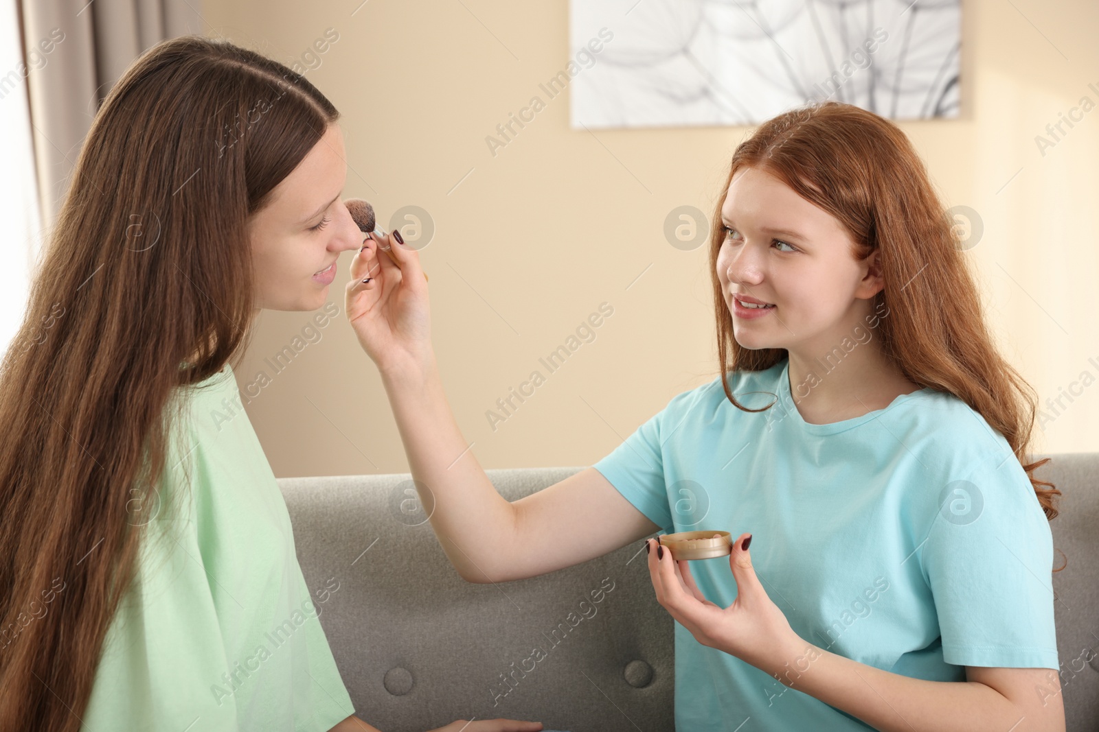 Photo of Teenage girl applying blush on her friend's face indoors