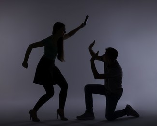 Photo of Domestic violence. Silhouette of woman with frying pan threatening her husband on grey background