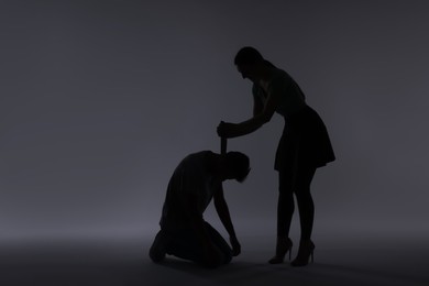 Photo of Domestic violence. Silhouette of woman with knife trying to kill her husband on grey background