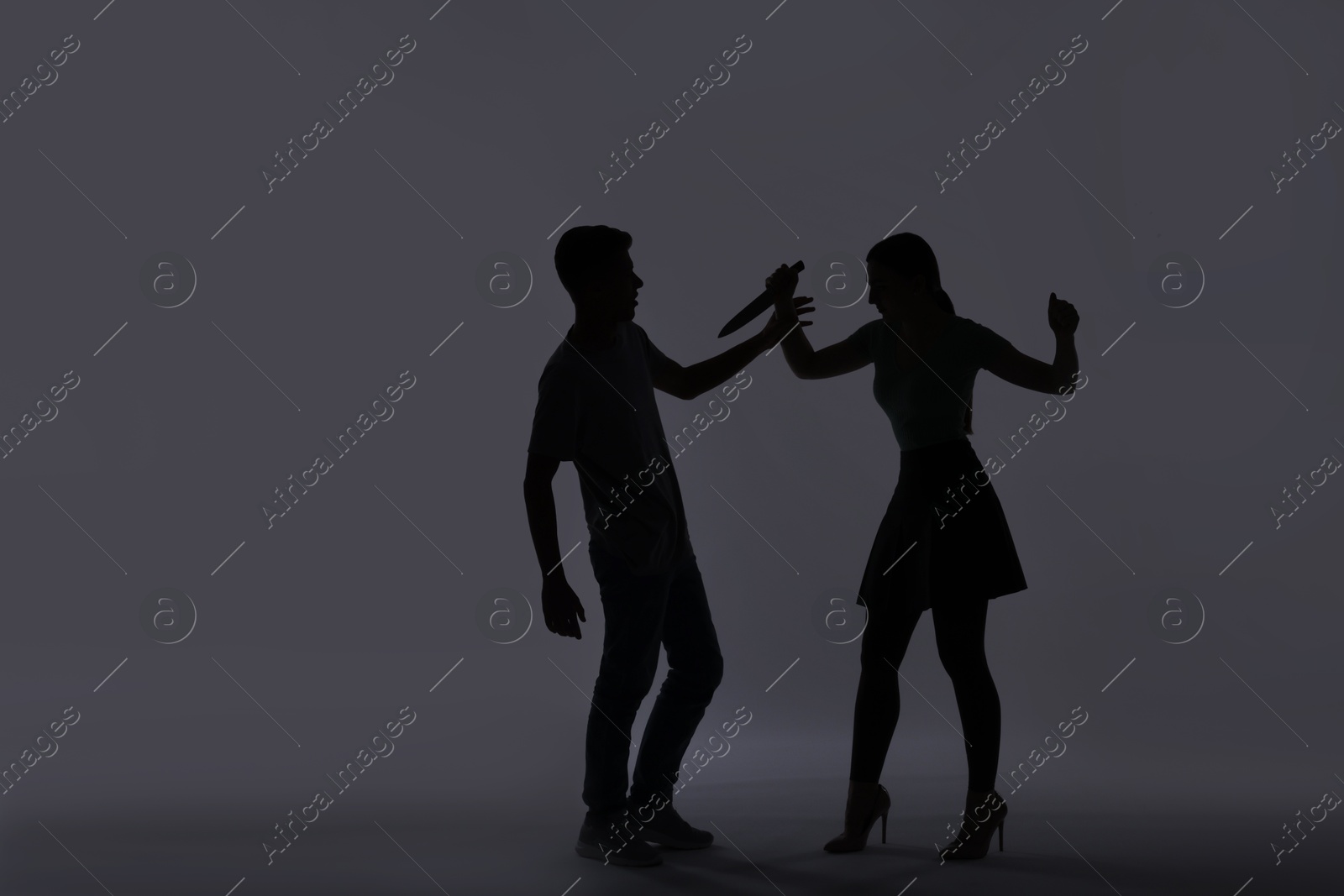 Photo of Domestic violence. Silhouette of woman with knife threatening her husband on grey background