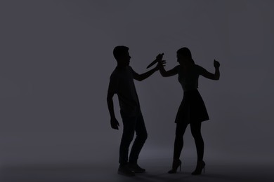 Photo of Domestic violence. Silhouette of woman with knife threatening her husband on grey background