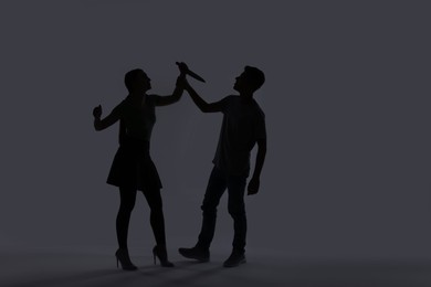 Photo of Domestic violence. Silhouette of woman with knife threatening her husband on grey background