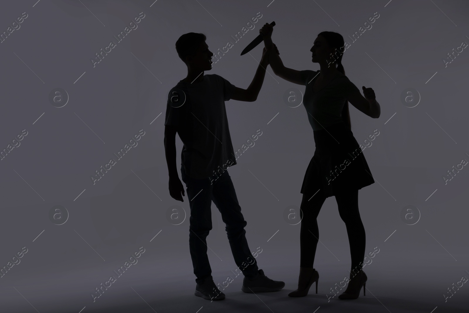 Photo of Domestic violence. Silhouette of woman with knife threatening her husband on grey background