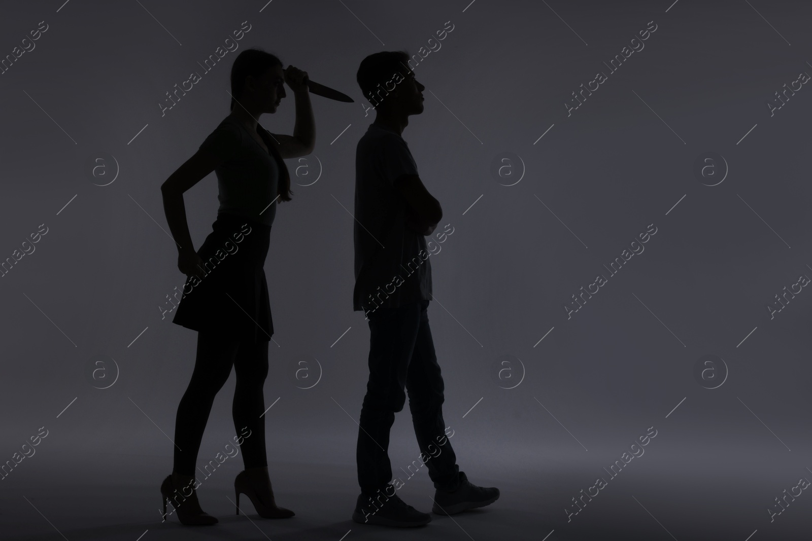 Photo of Domestic violence. Silhouette of woman with knife trying to kill her husband on grey background