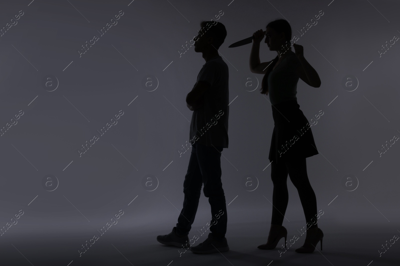 Photo of Domestic violence. Silhouette of woman with knife trying to kill her husband on grey background