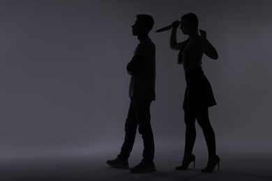 Photo of Domestic violence. Silhouette of woman with knife trying to kill her husband on grey background