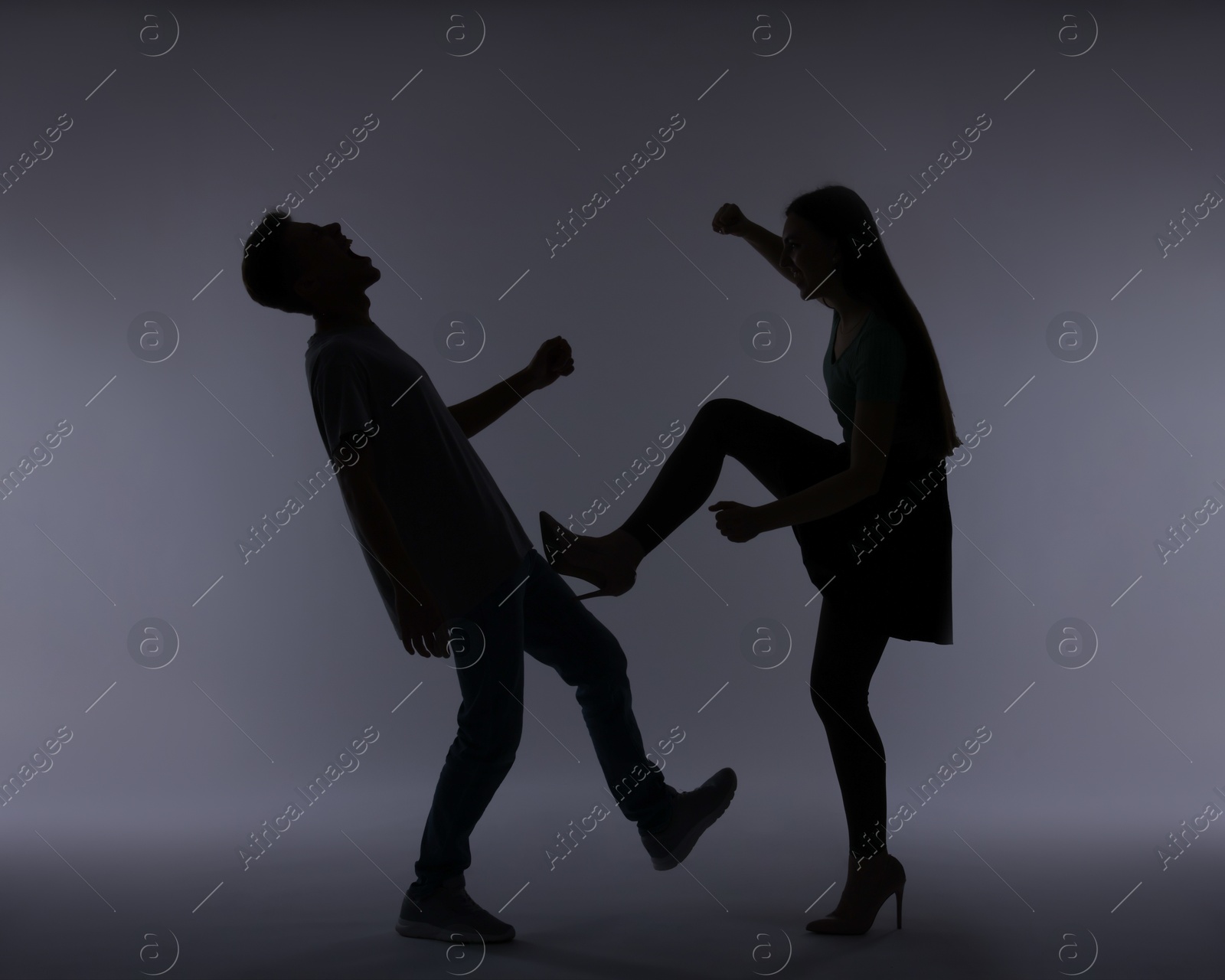 Photo of Domestic violence. Silhouette of woman kicking her husband on grey background