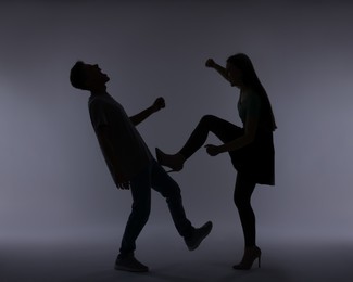 Photo of Domestic violence. Silhouette of woman kicking her husband on grey background