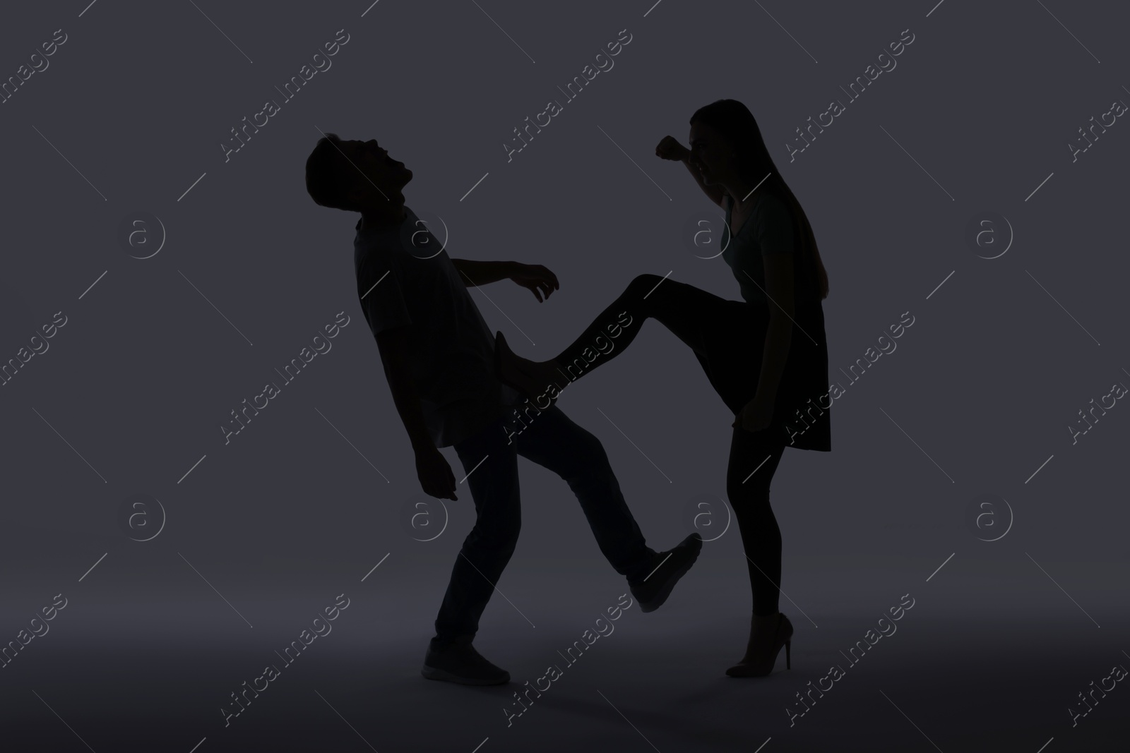 Photo of Domestic violence. Silhouette of woman kicking her husband on grey background