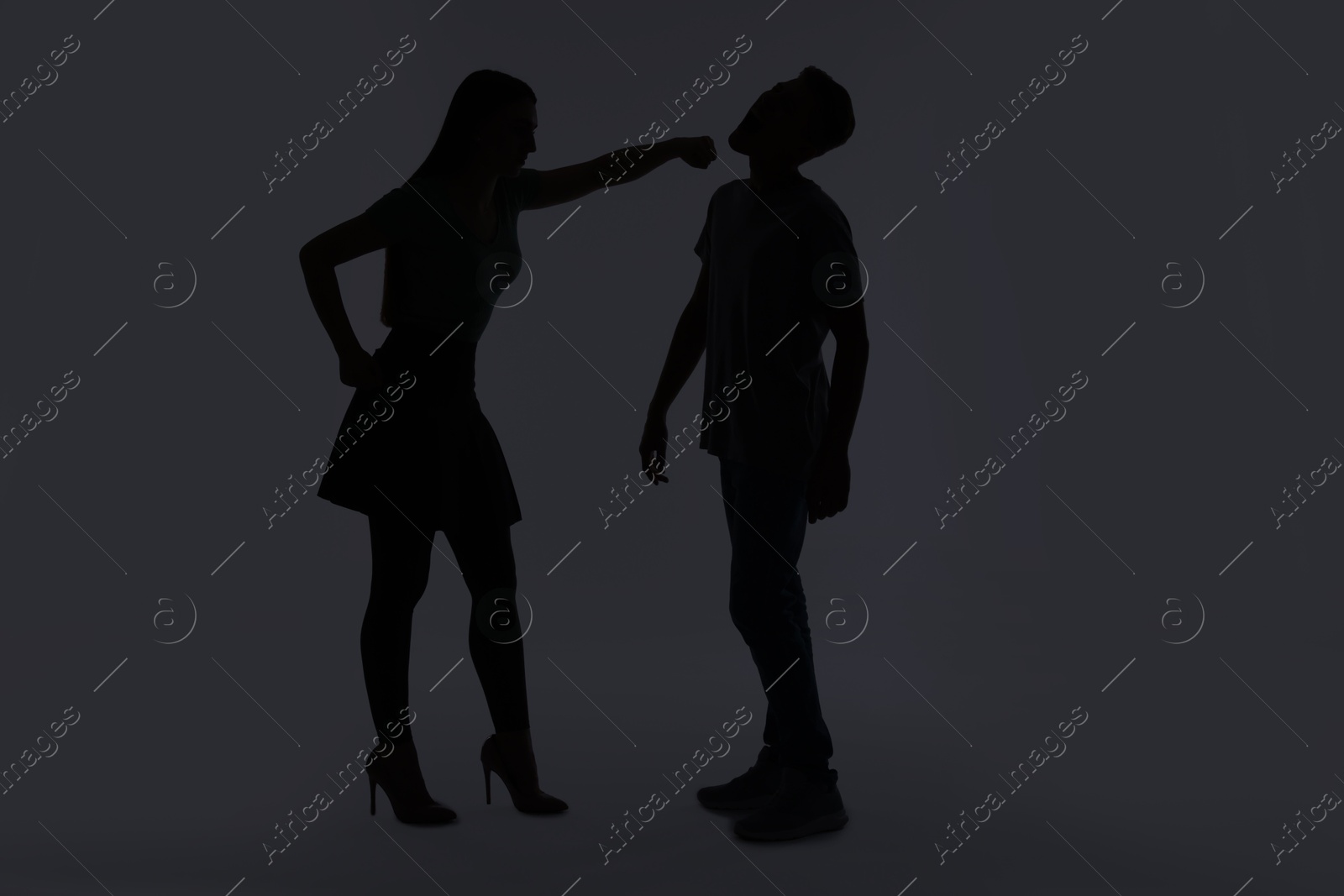 Photo of Domestic violence. Silhouette of woman punching her husband on grey background