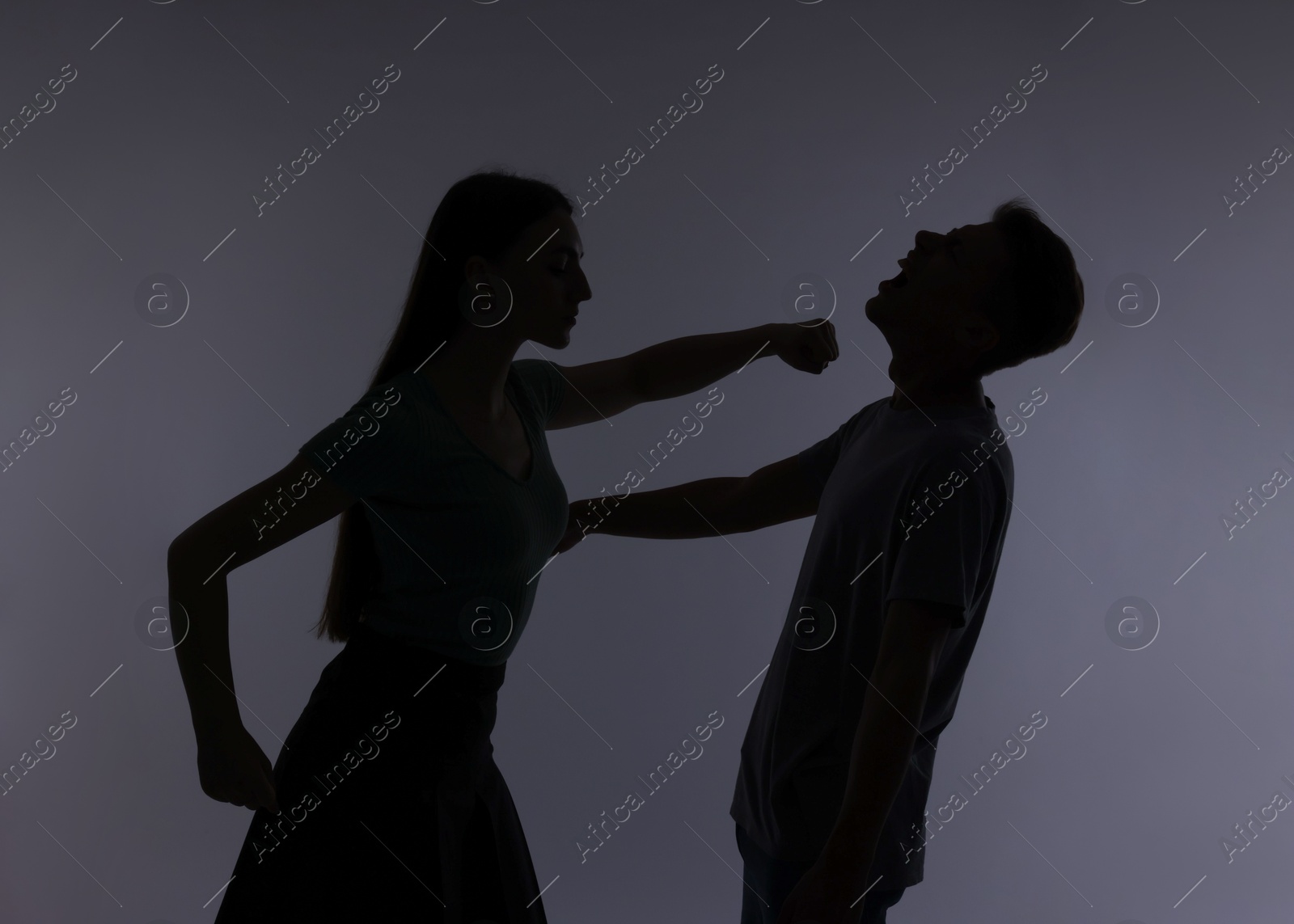 Photo of Domestic violence. Silhouette of woman punching her husband on grey background