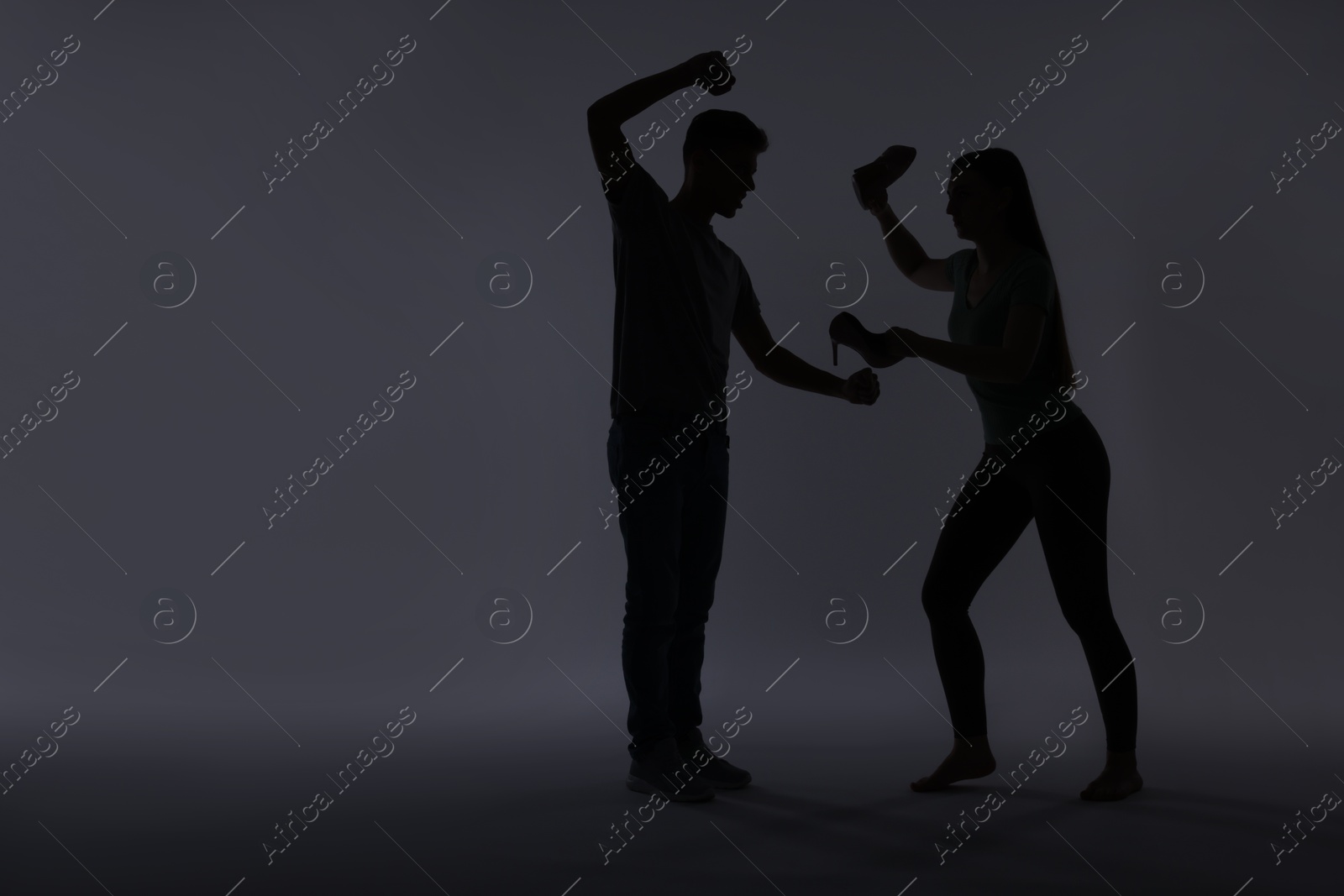 Photo of Domestic violence. Silhouette of man threatening his wife on grey background