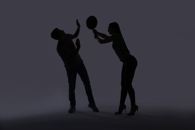 Photo of Domestic violence. Silhouette of woman with frying pan threatening her husband on grey background