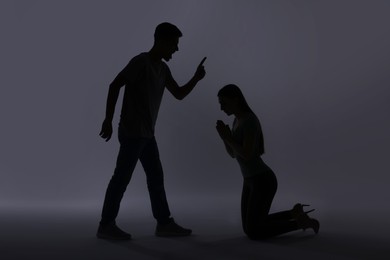 Photo of Domestic violence. Silhouette of man threatening his wife on grey background