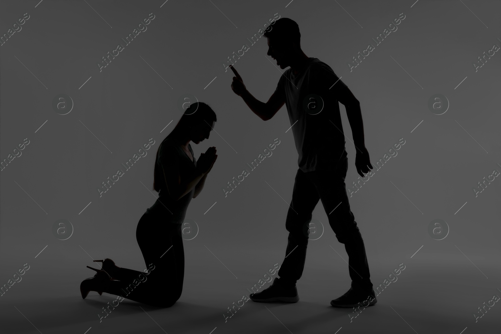 Photo of Domestic violence. Silhouette of man threatening his wife on grey background