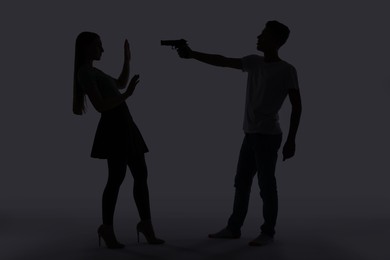 Photo of Domestic violence. Silhouette of man with gun threatening his wife on grey background