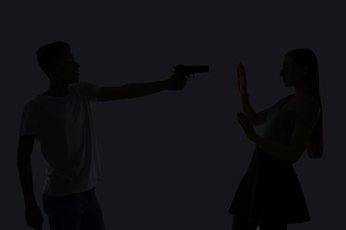 Photo of Domestic violence. Silhouette of man with gun threatening his wife on grey background