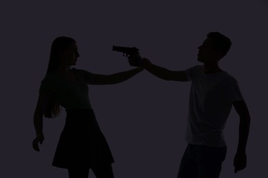 Photo of Domestic violence. Silhouette of man with gun threatening his wife on grey background