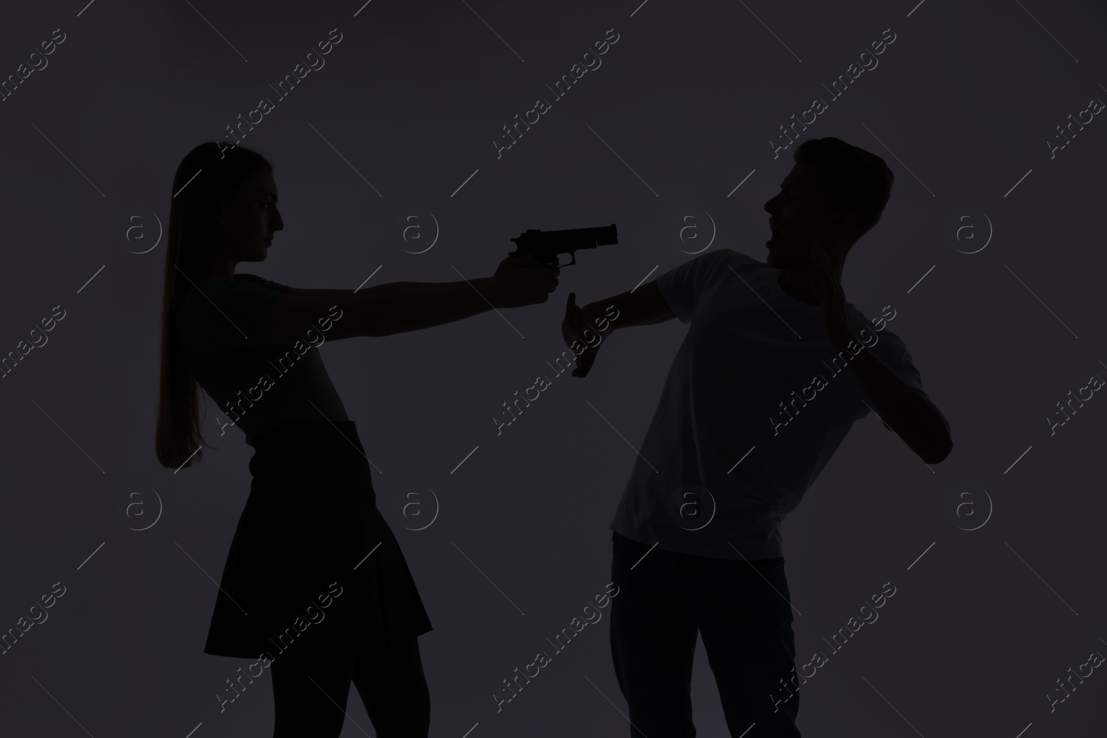 Photo of Domestic violence. Silhouette of woman with gun threatening her husband on grey background