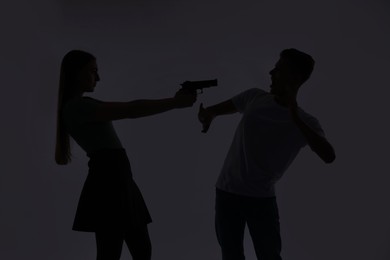 Photo of Domestic violence. Silhouette of woman with gun threatening her husband on grey background