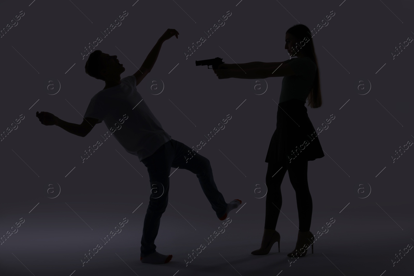 Photo of Domestic violence. Silhouette of woman with gun threatening her husband on grey background