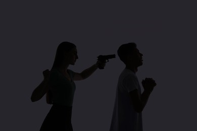 Photo of Domestic violence. Silhouette of woman with gun threatening her husband on grey background