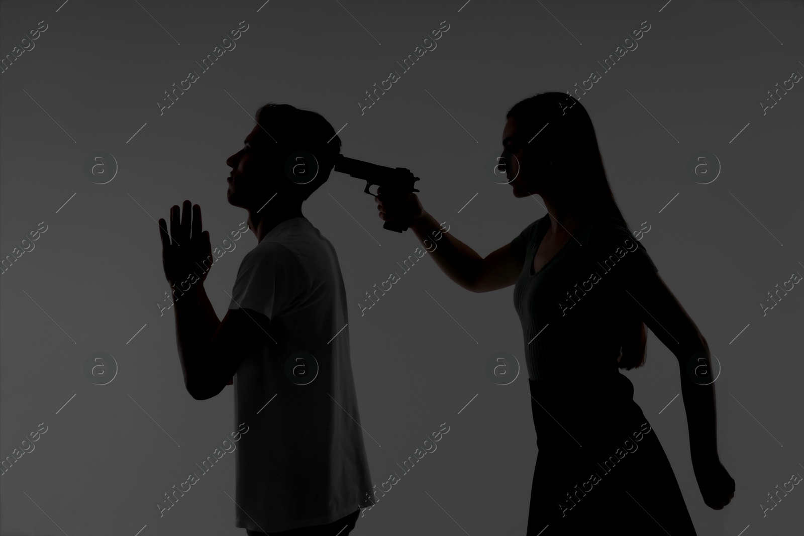 Photo of Domestic violence. Silhouette of woman with gun threatening her husband on grey background