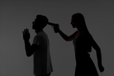 Photo of Domestic violence. Silhouette of woman with gun threatening her husband on grey background