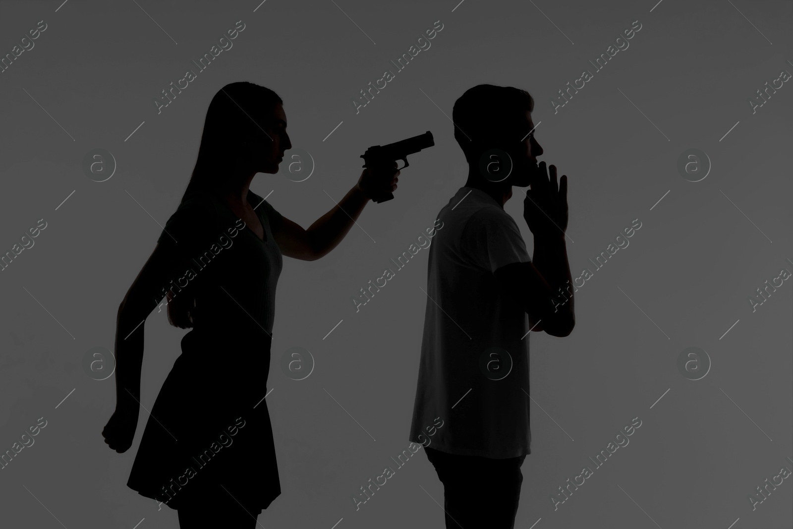 Photo of Domestic violence. Silhouette of woman with gun threatening her husband on grey background