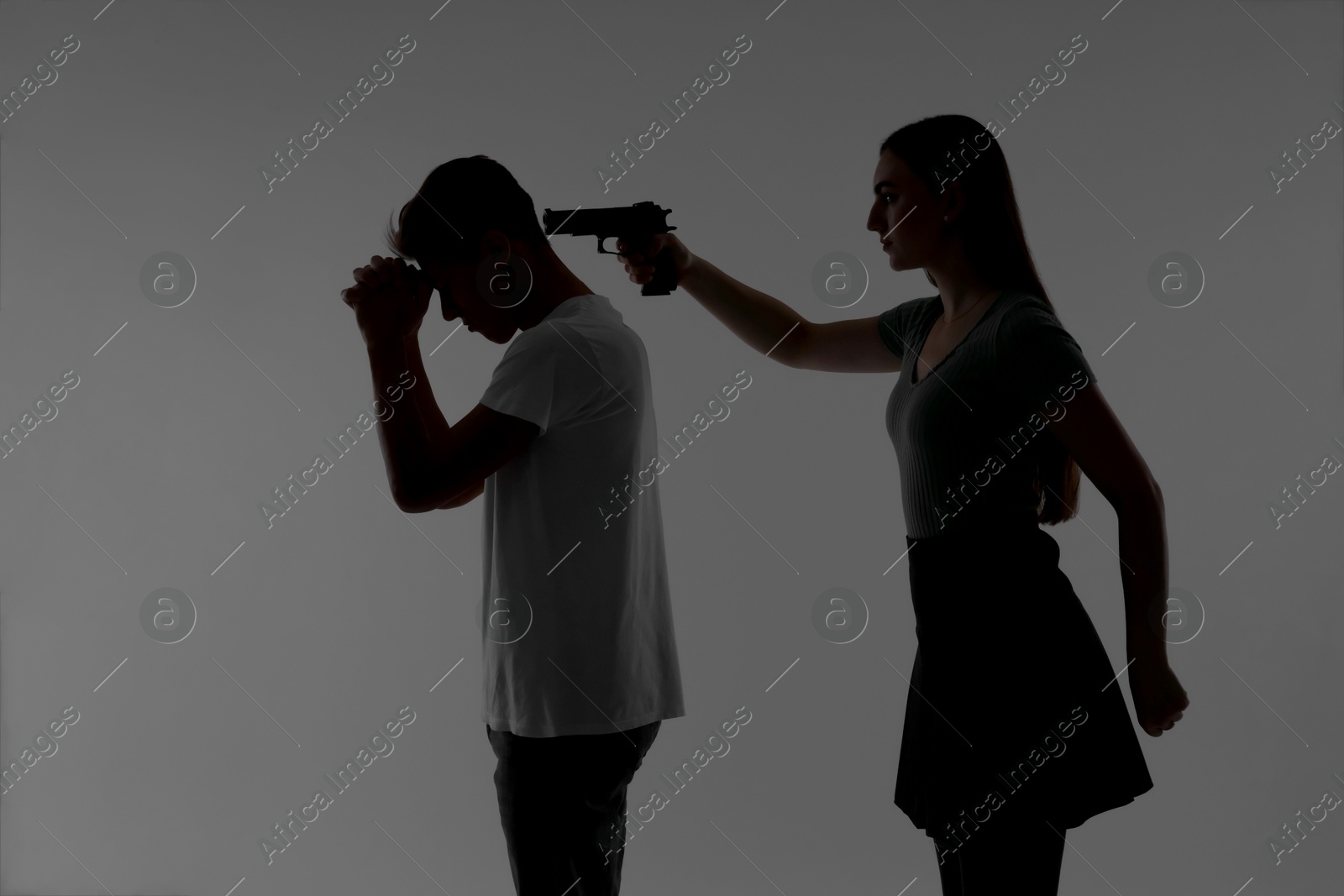 Photo of Domestic violence. Silhouette of woman with gun threatening her husband on grey background