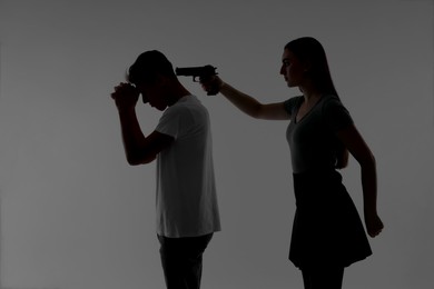 Photo of Domestic violence. Silhouette of woman with gun threatening her husband on grey background