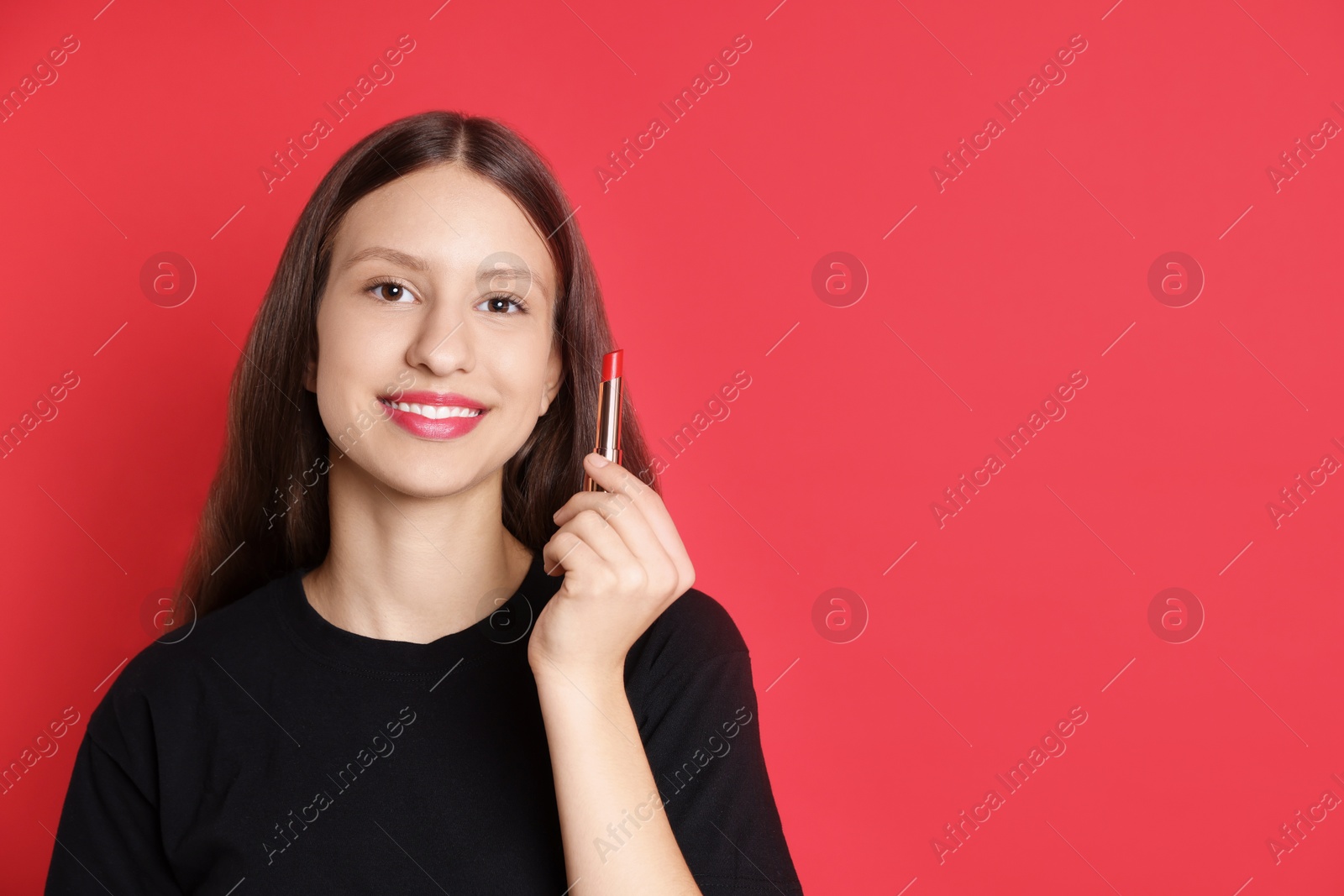 Photo of Smiling teenage girl with lipstick on red background. Space for text