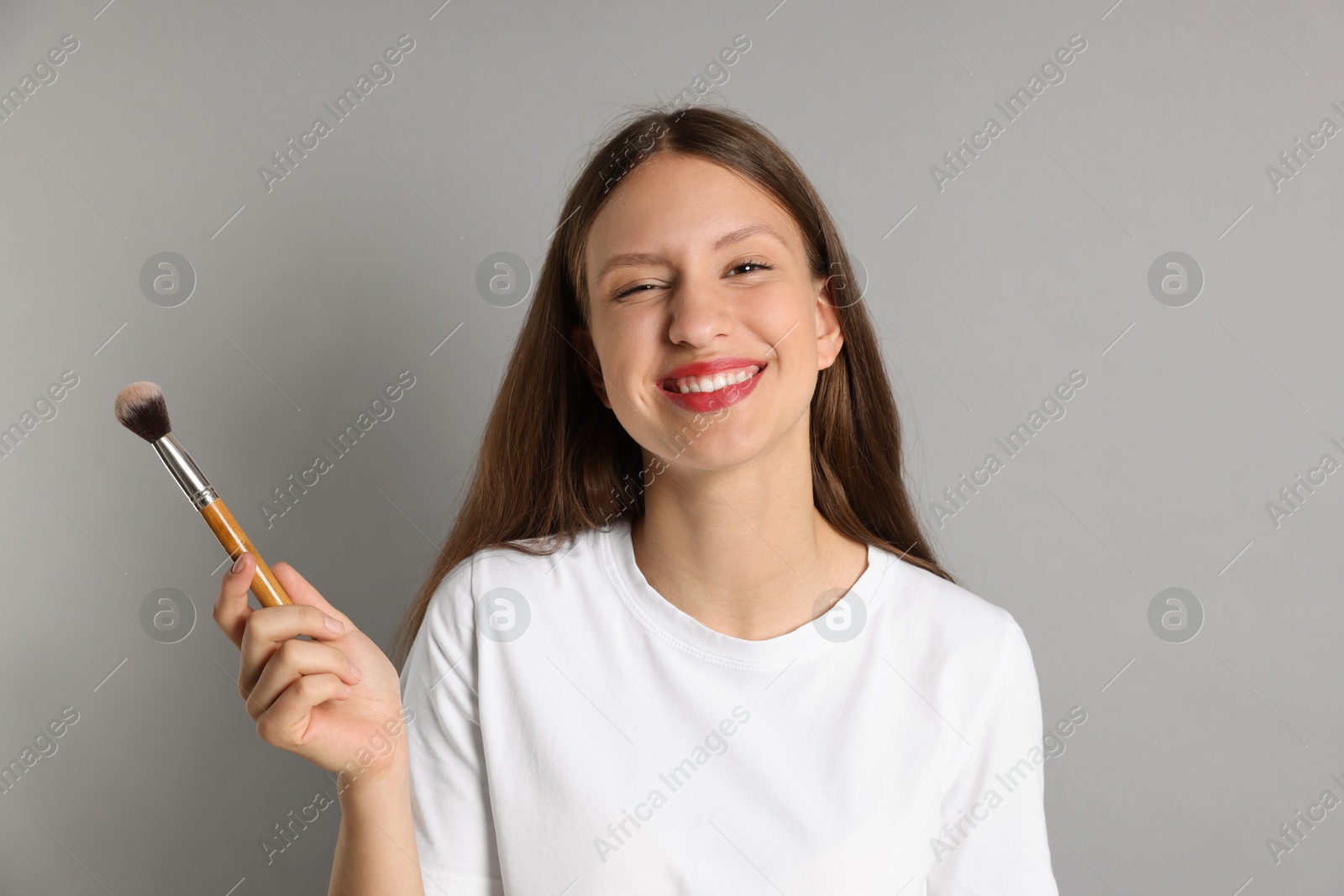 Photo of Smiling teenage girl with makeup brush on grey background