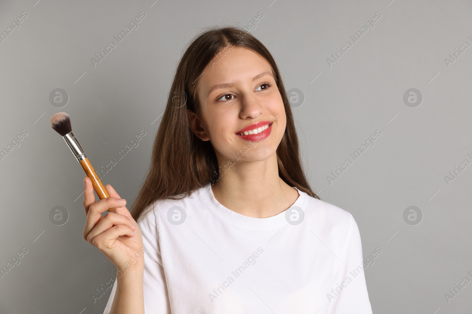 Photo of Smiling teenage girl with makeup brush on grey background