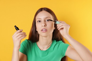 Photo of Teenage girl applying mascara on yellow background