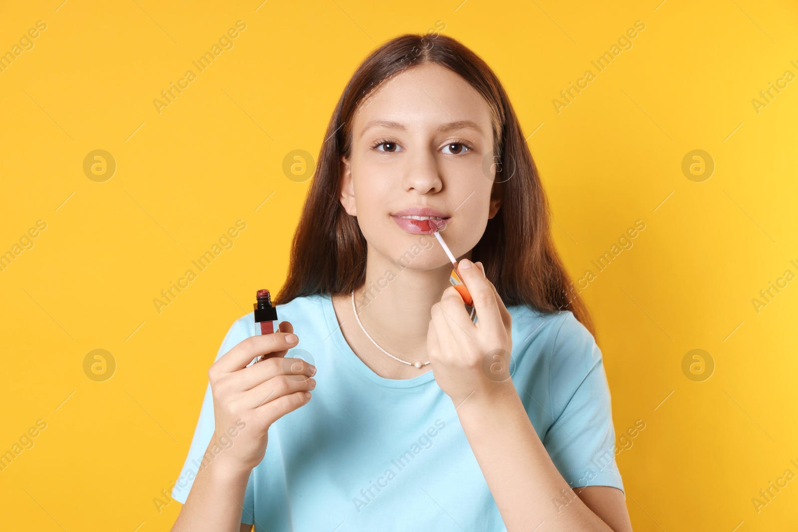 Photo of Teenage girl applying lip gloss on yellow background