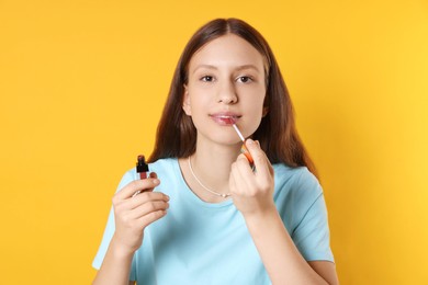 Photo of Teenage girl applying lip gloss on yellow background